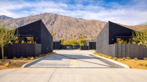 Un edificio moderno con fachada simétrica, una entrada central y vistas a montañas al fondo.