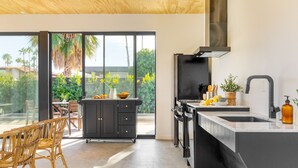 Cocina moderna con una isla grande, armarios negros y vistas a un patio con mobiliario exterior.