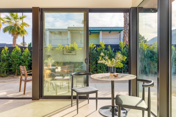 Une terrasse moderne avec une porte vitrée donnant sur un jardin, comprenant une table ronde et deux chaises.