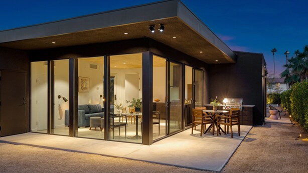 Una casa moderna con un patio con paredes de cristal, un comedor y una cocina visibles a través del vidrio.