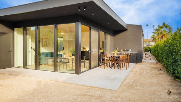Una casa moderna amb un ampli patí de vidre, una zona de dinar i un jardí ben cuidat.