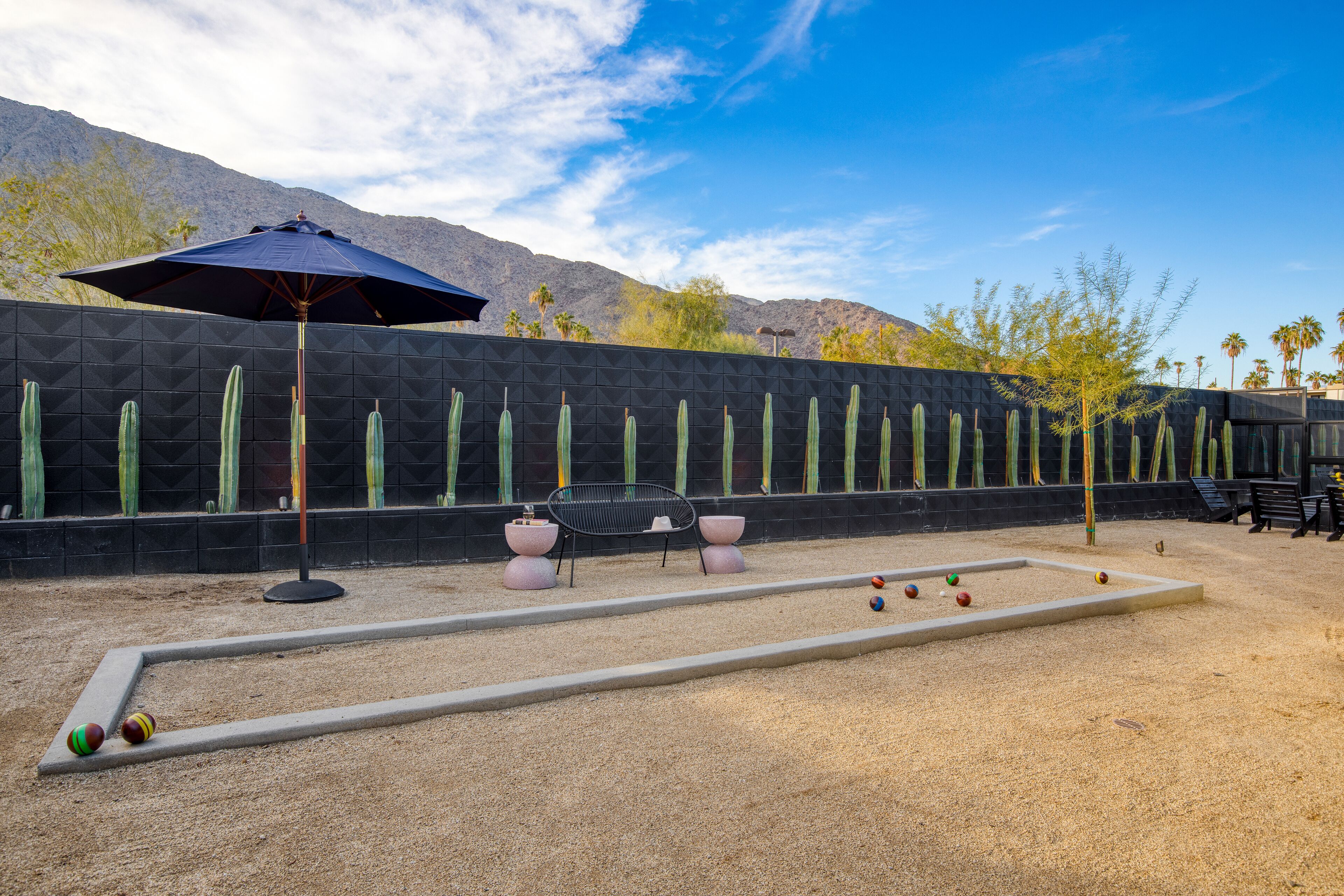 A courtyard with a croquet set, a black umbrella, and a cactus wall.