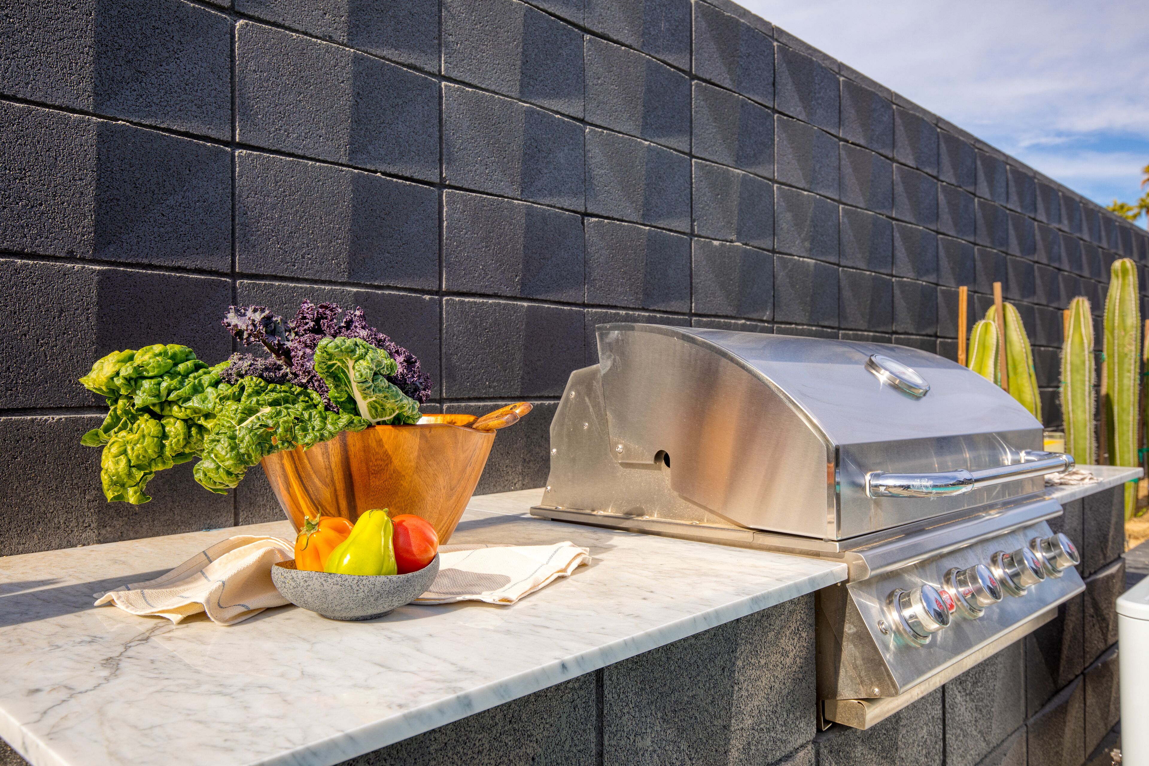 A barbecue grill with a stainless steel finish, a marble countertop, and a black tiled backsplash.