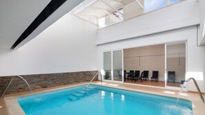 En inomhuspool med en vägg av sten, en glasdörr som leder till en sittgrupp och ett högt tak.