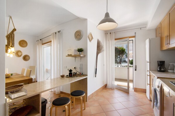 A modern kitchen with a dining area, a washing machine, and a large window.