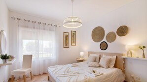 Ett sovrum med en säng, en stol, ett sängbord med en lampa, en spegel och dekorationer på väggen.