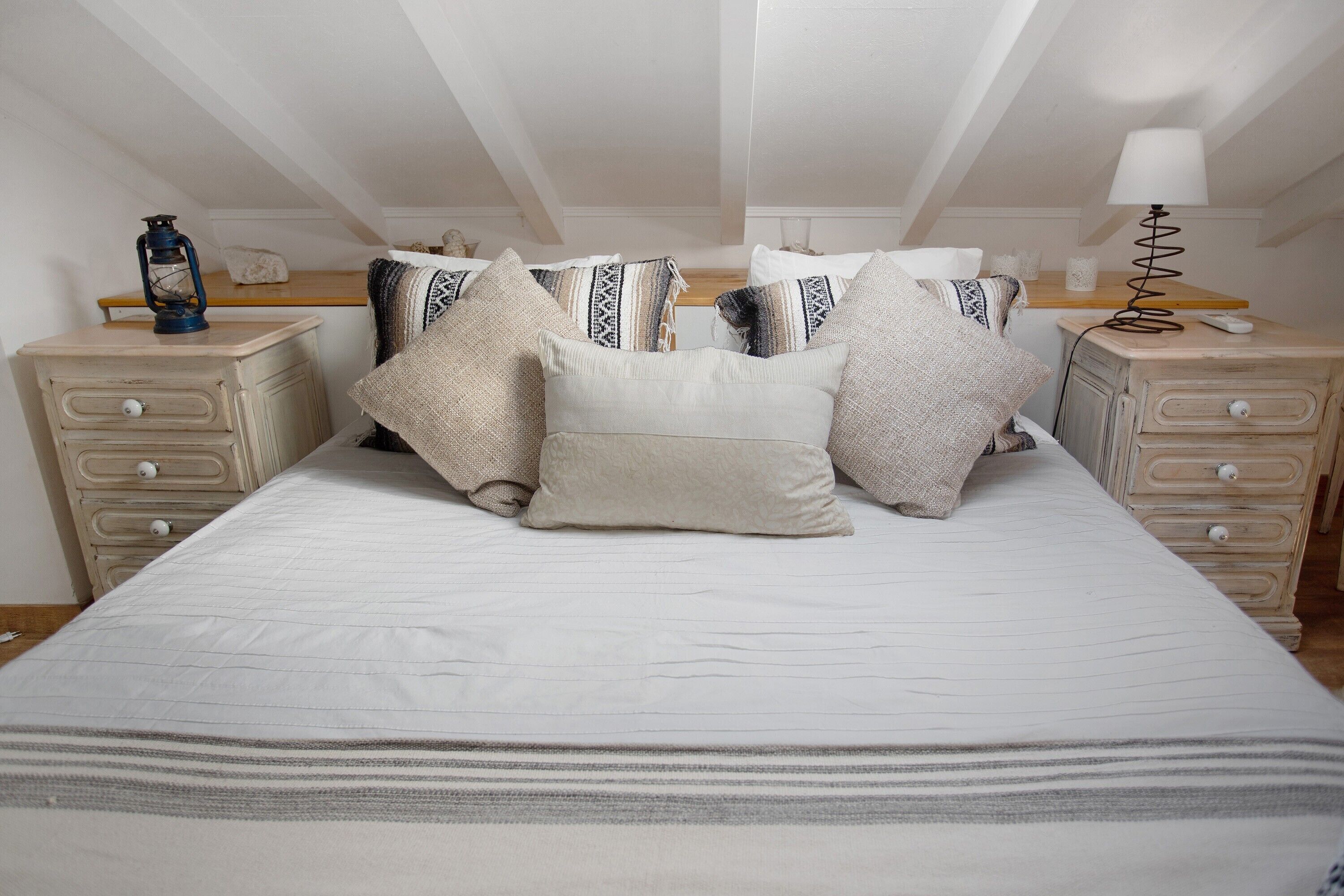 A bedroom with a large bed, two bedside tables, a lamp, and a lantern.