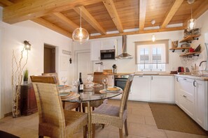 A modern kitchen with white cabinets, a glass dining table, wicker chairs, and wooden ceiling beams. - Holiday Home 'Holi' with Private Pool, Wi-Fi and Air Conditioning (Valada)