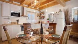 A kitchen with white cabinets, a glass dining table, wicker chairs, and a hanging light fixture. - Holiday Home 'Holi' with Private Pool, Wi-Fi and Air Conditioning (Valada)