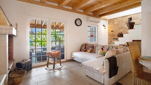 A cozy living room with a sofa, a chair, a fireplace, a clock, and a view through a glass door. - Holiday Home 'Holi' with Private Pool, Wi-Fi and Air Conditioning (Valada)