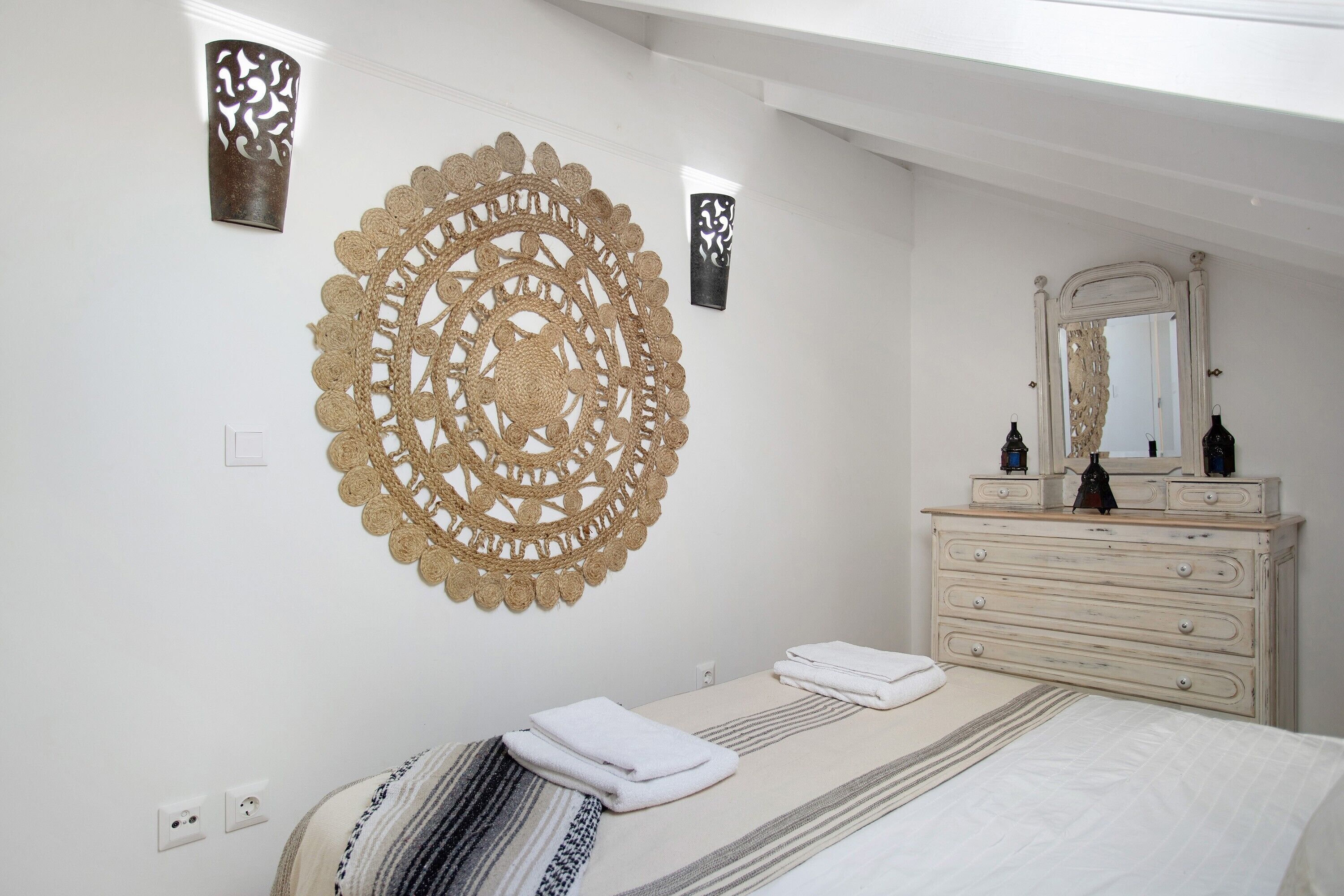 Une chambre à coucher comprenant un lit, une commode, un miroir et des œuvres d’art décoratives accrochées au mur.
