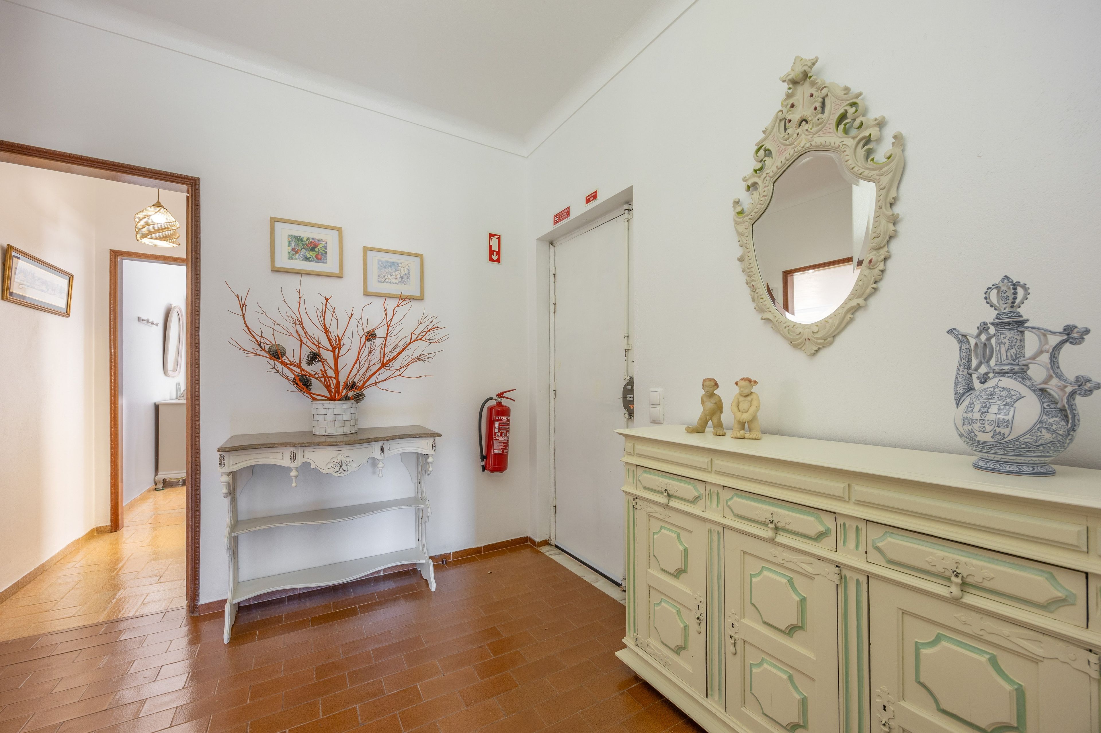 Um corredor com um espelho, um aparador branco e um armário decorado com objetos.