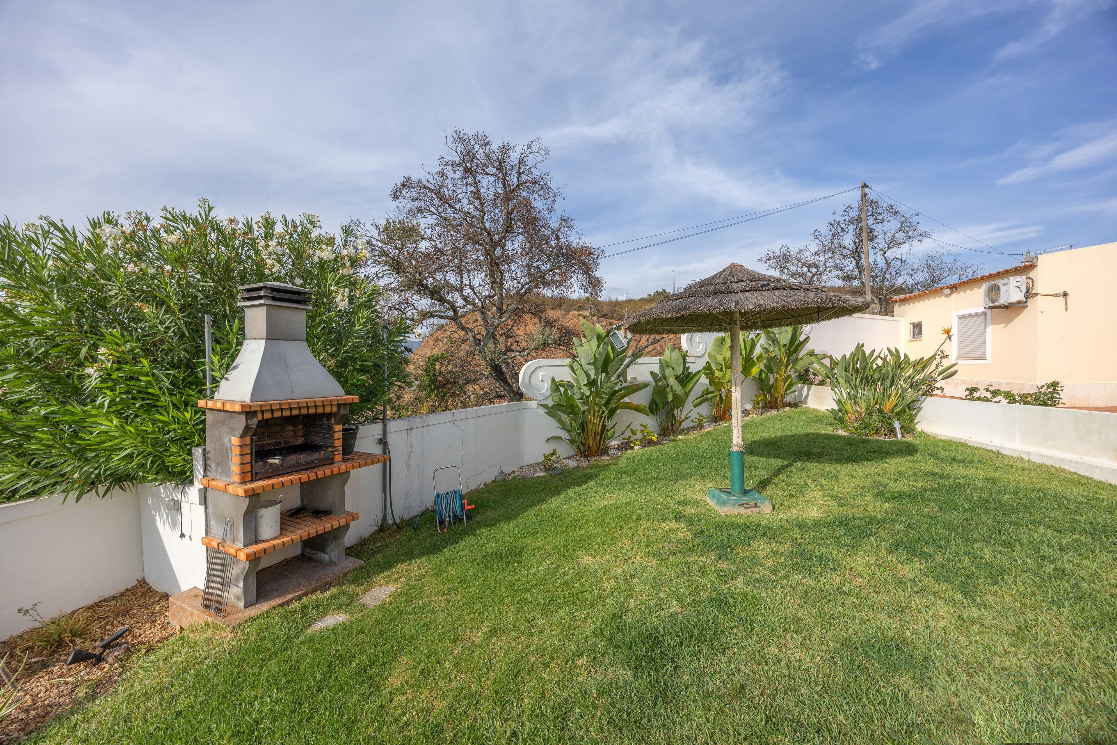 A backyard with a brick barbecue grill, a small umbrella, and a grassy lawn.