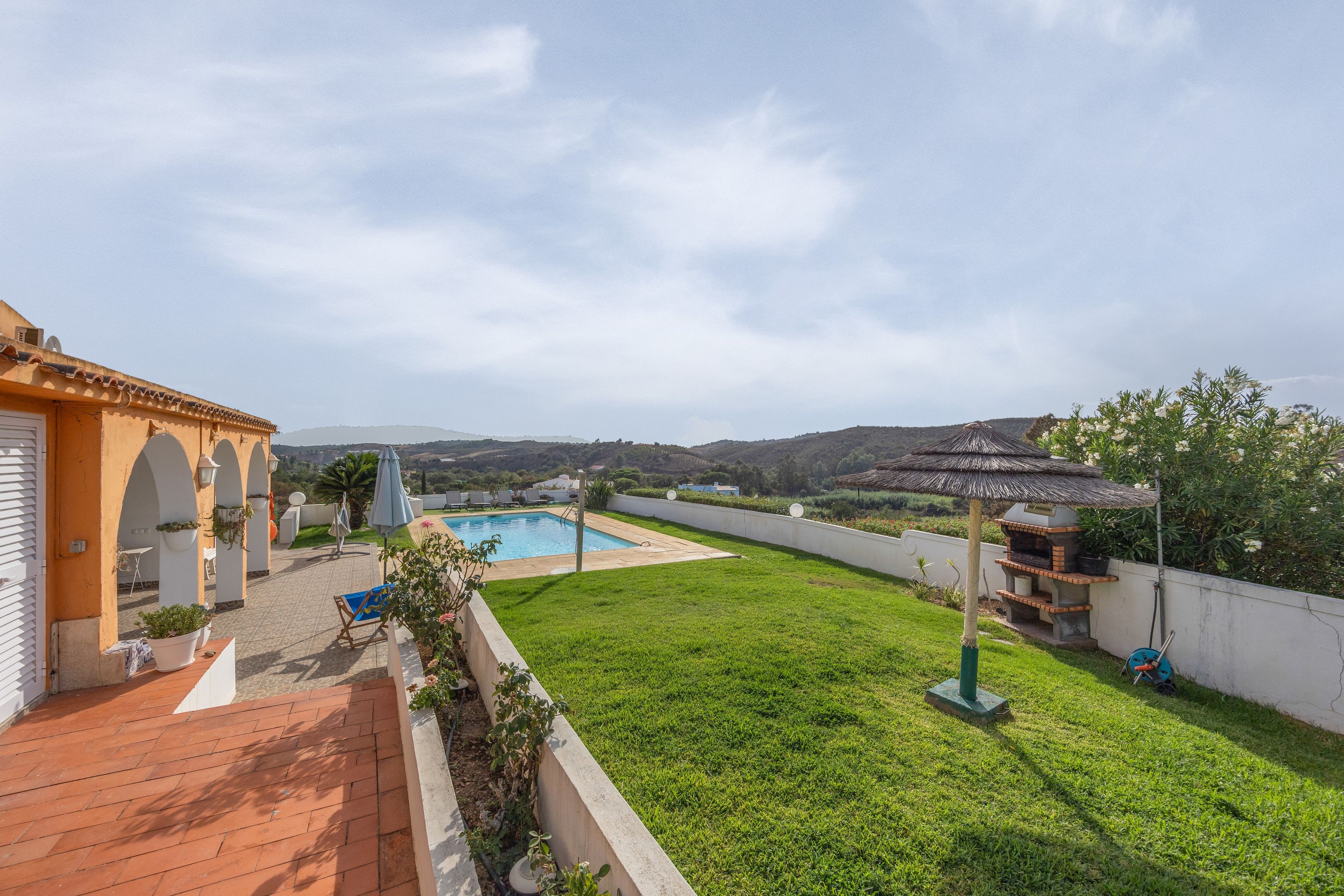 Un jardin avec une piscine, un espace barbecue et une vue sur les collines.