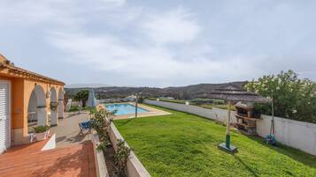 Un jardin avec une piscine, un espace barbecue et une vue sur les collines.