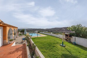 A backyard with a swimming pool, a barbecue area, and a view of the hills.