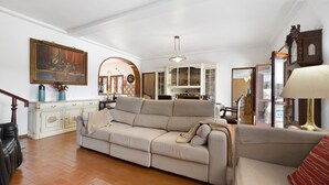 Una sala de estar con un sofá color beige, un mueble de madera, un cuadro y un comedor al fondo.