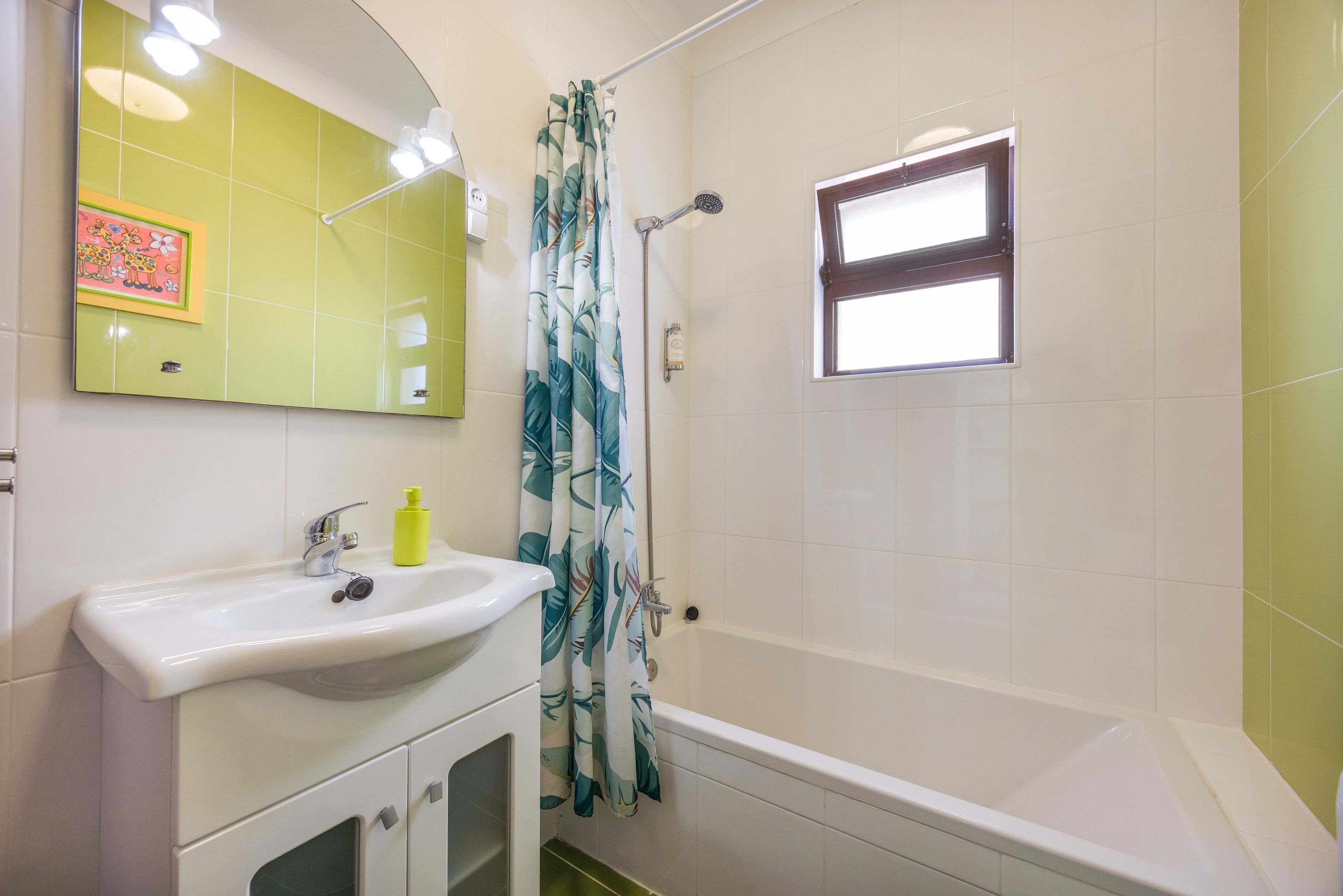 A bathroom with a white sink, a mirror, a shower curtain with a leaf pattern, and a window.