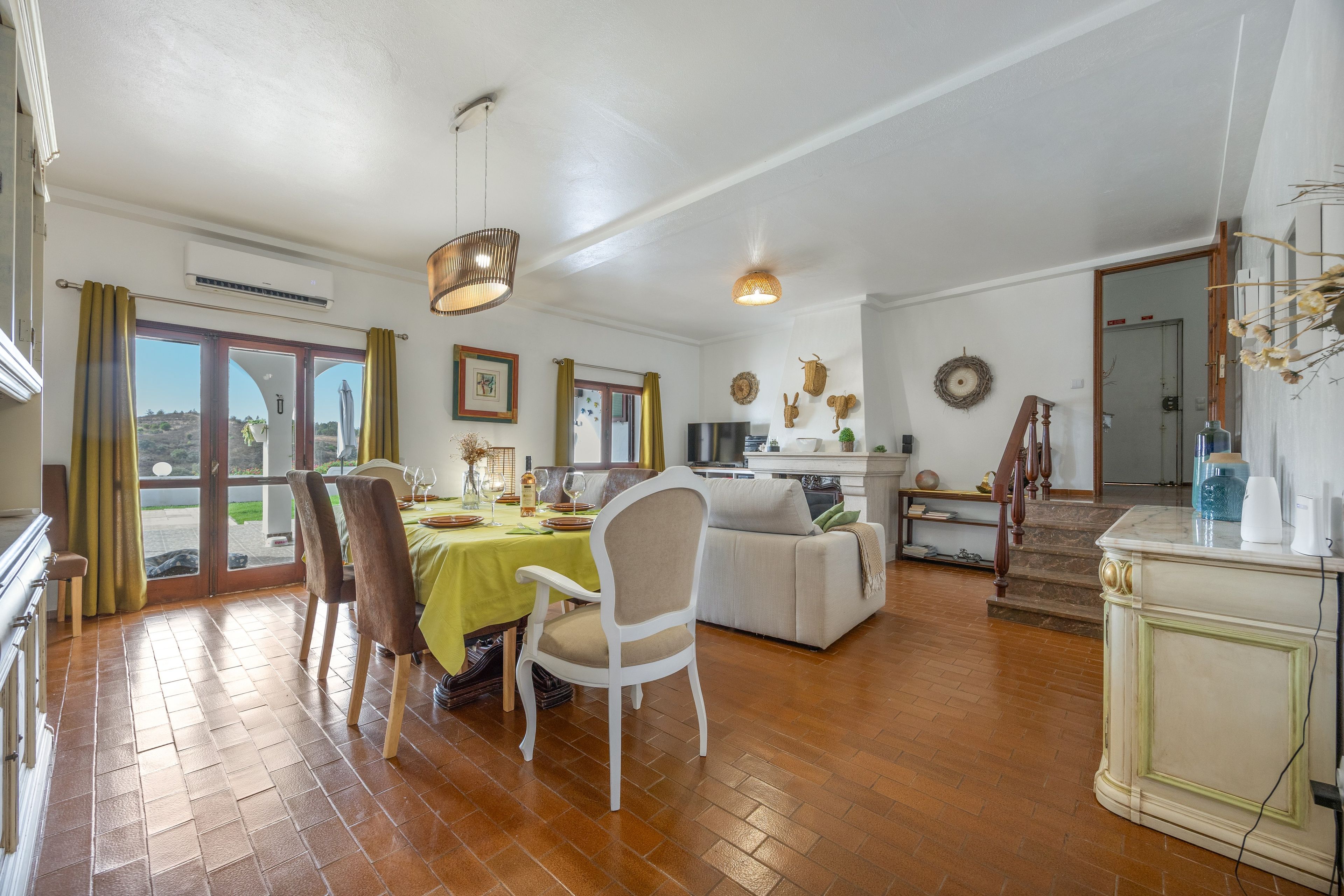A spacious living area with a dining table set for four, a sofa, and a staircase leading to an upper floor.