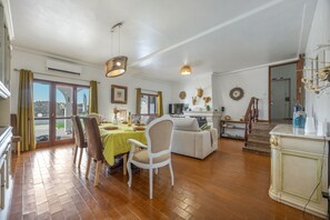 A spacious living area with a dining table set for four, a sofa, and a staircase leading to an upper floor.