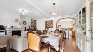 Un comedor con chimenea, sillas de madera, una mesa blanca y una cocina al fondo.