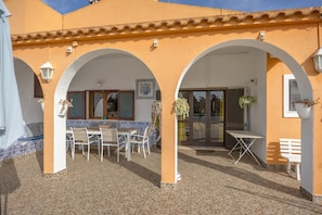 Ein Gebäude mit einer mit Fliesen belegten Terrasse, weißen Möbeln und Bögen.
