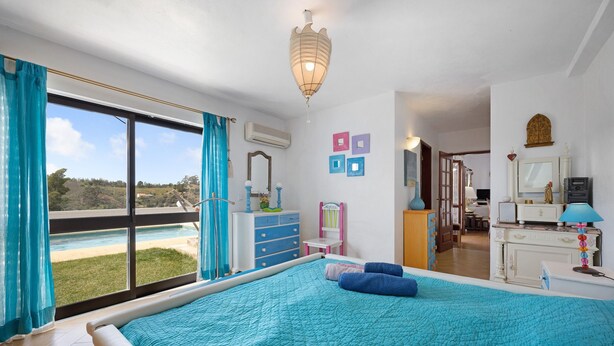 Un dormitorio con una cama grande, vista a una piscina y un baño con espejo y cómoda.