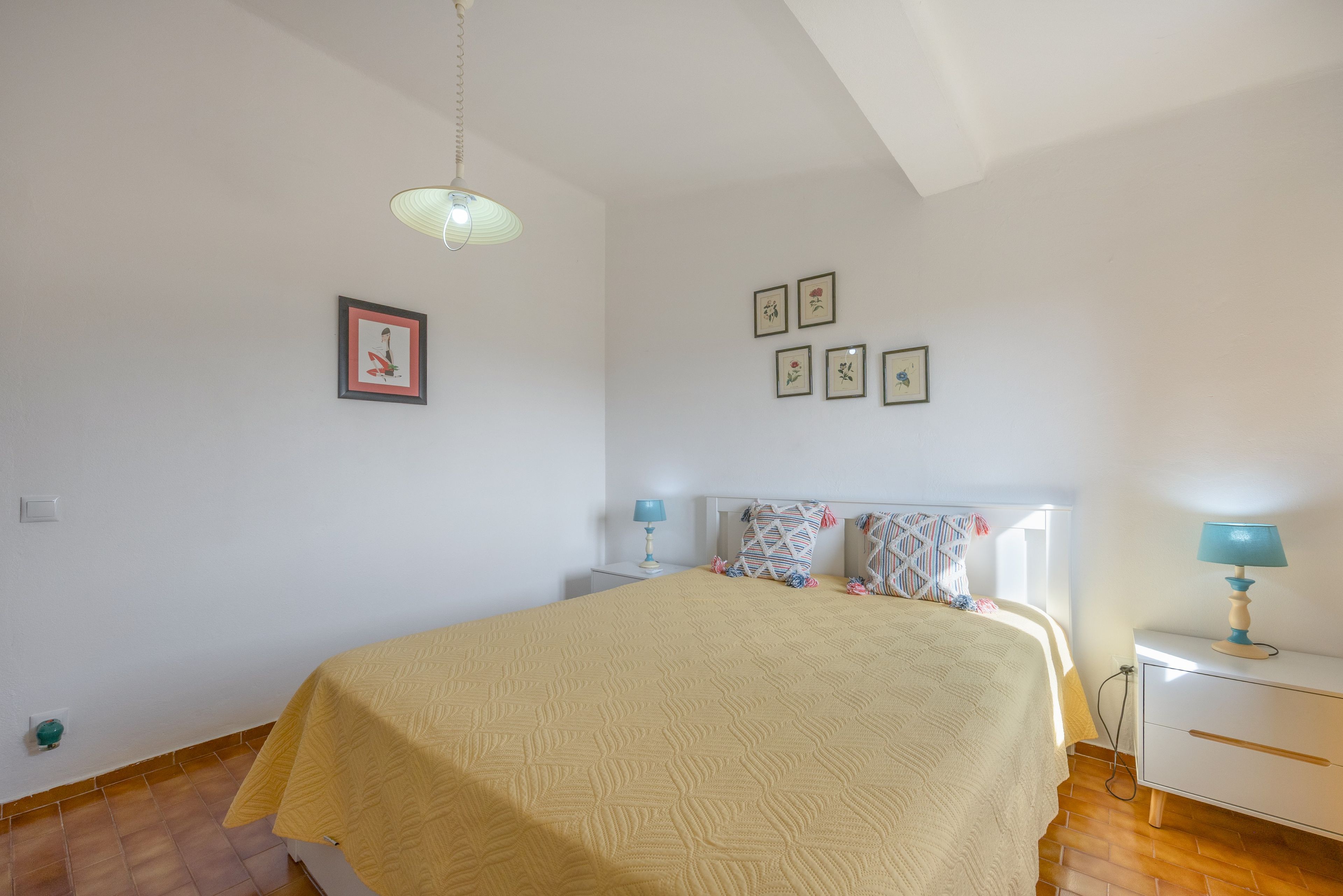 A bedroom with a bed, bedside tables, a lamp, and wall-mounted pictures.