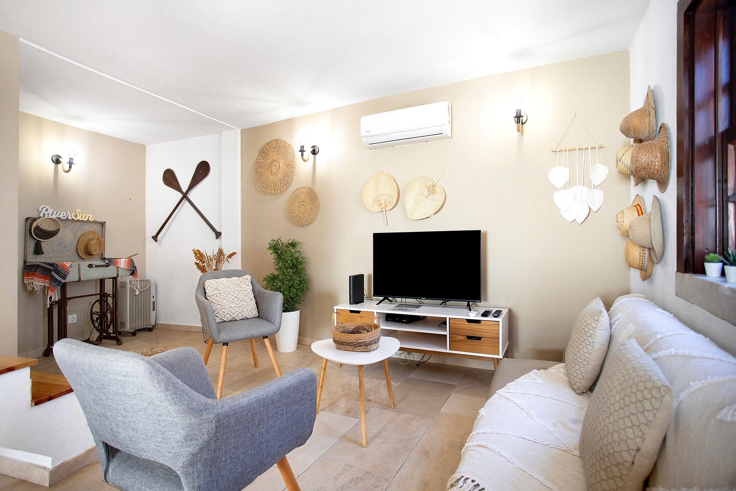 A living room with a sofa, a chair, a TV, and wall decorations including paddles and hats.