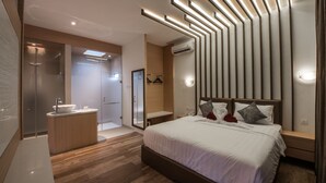 A modern bedroom with a large bed, bedside tables, a built-in wardrobe, a vanity with a mirror, and a shower area. - Woda Villa & Spa (Batam)