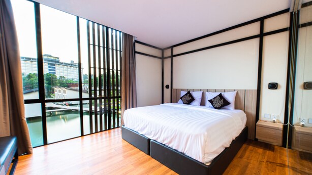 Een moderne slaapkamer met een groot bed, houten vloeren en een stadsgezicht door ramen van vloer tot plafond.