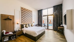 A modern hotel room with a large bed, a desk, a TV, and a view of the pool. - Woda Villa & Spa (Batam)