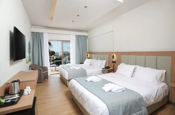 A hotel room with two beds, a desk, a chair, a TV, and a balcony with a view. - Flegra Palace Hotel & Spa (Kassandra)