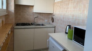 Una cocina compacta con estufa a gas, lavamanos y un refrigerador pequeño.