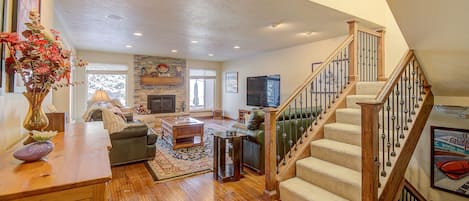 A spacious living room with a fireplace, a staircase, and a view of the outdoors.