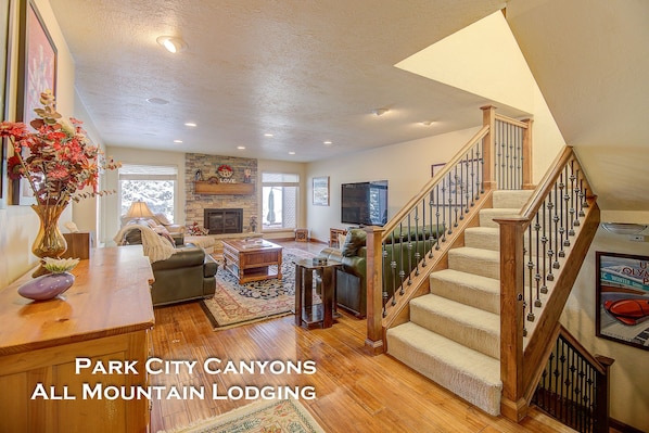 A spacious living room with a fireplace, a staircase, and a view of the outdoors.