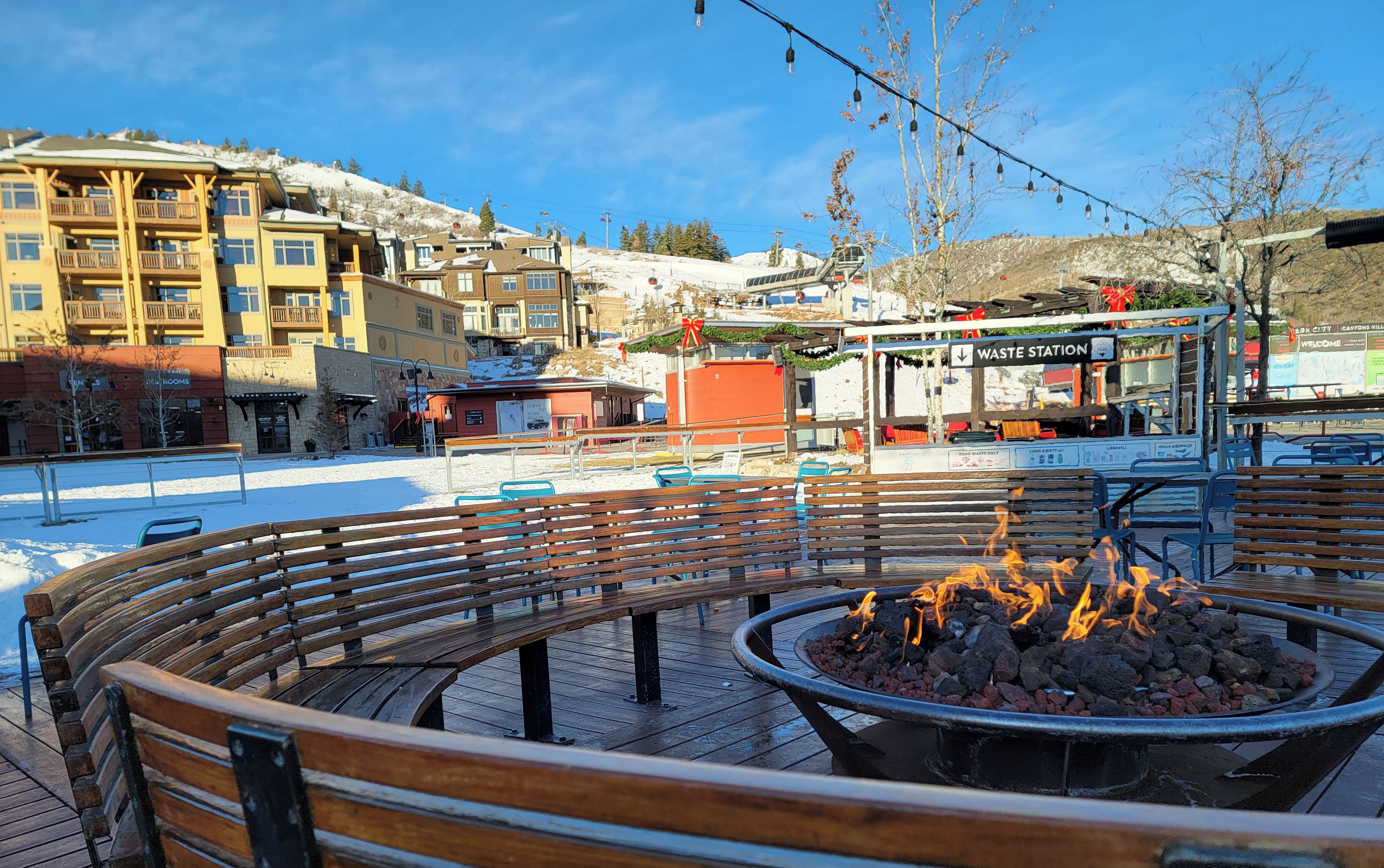 A wooden deck with a fire pit, benches, and a view of a mountain lodge with a ski lift in the background.