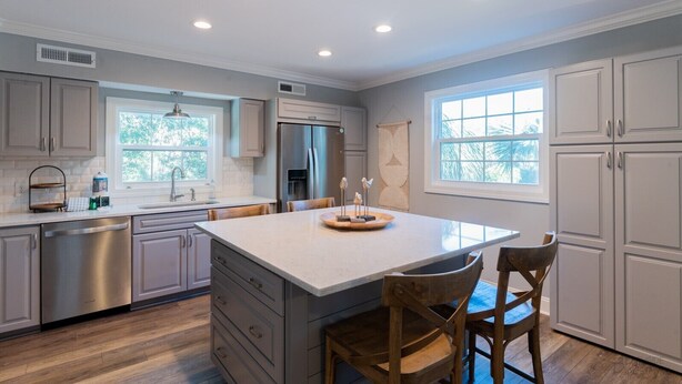 A modern kitchen with grey cabinets, a stainless steel refrigerator, a large island with chairs, and a window providing natural light. - 1 Sea Hawk Lane - 5 Bedroom, 5th Row, Pet Friendly! (Hilton Head Island)