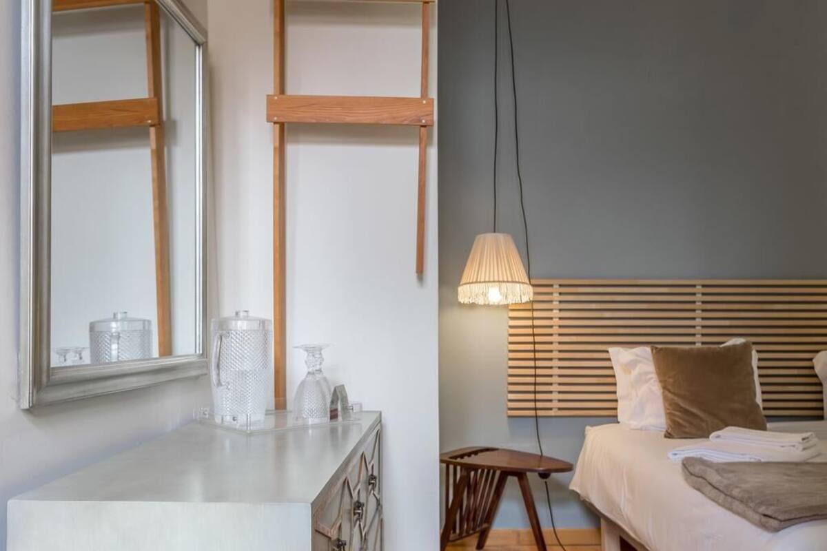 A bedroom with a bed, bedside table, lamp, and a mirror.