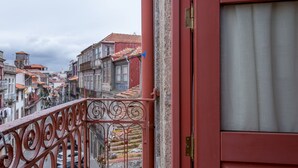 A red door with a metal balcony railing overlooking a cityscape with terracotta-roofed buildings. - The Poets Inn (Porto)