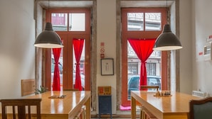 A dining area with wooden tables and chairs, red curtains, and a radio on a small cabinet. - The Poets Inn (Porto)