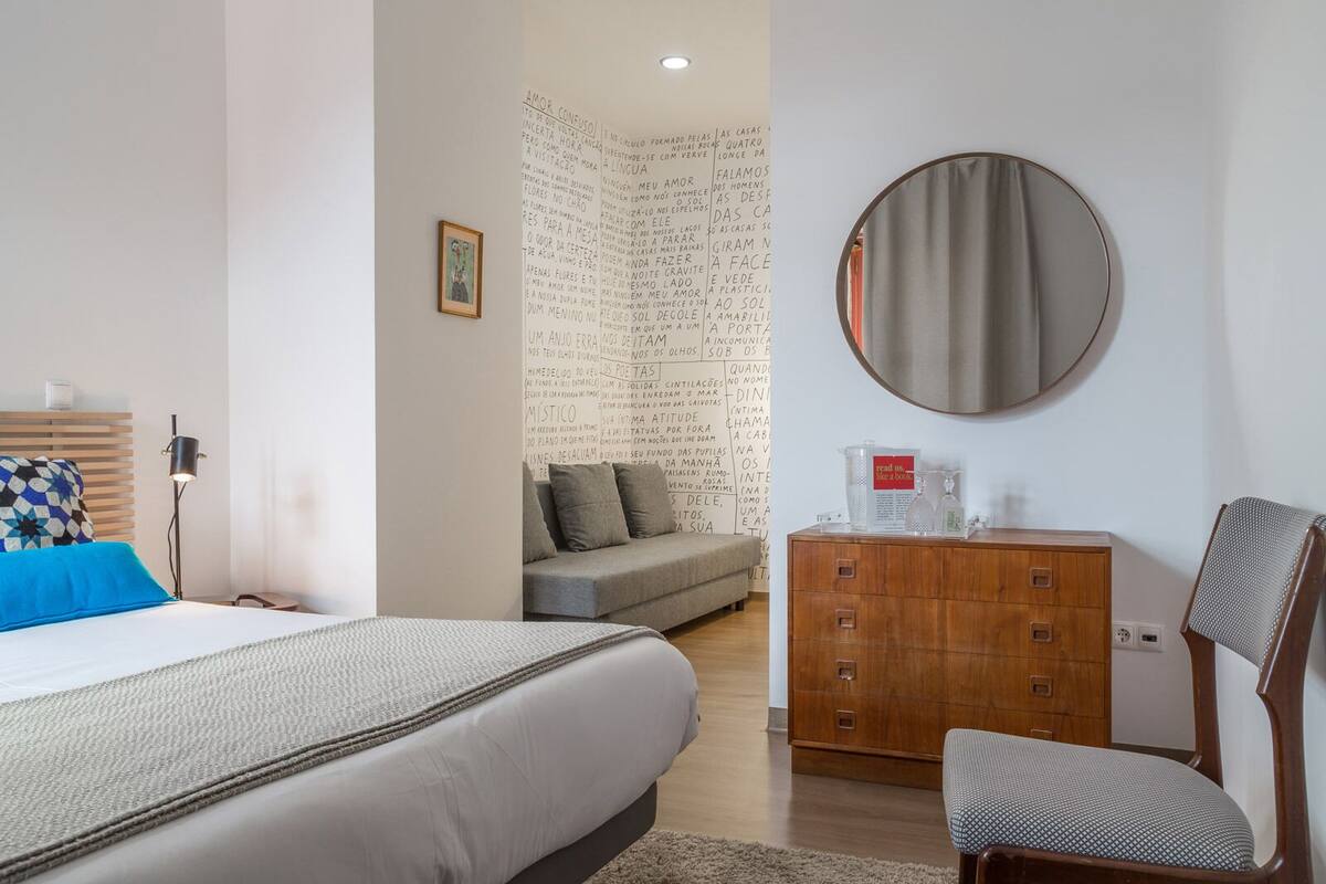 A bedroom with a bed, a wooden dresser, a chair, and a round mirror on the wall.