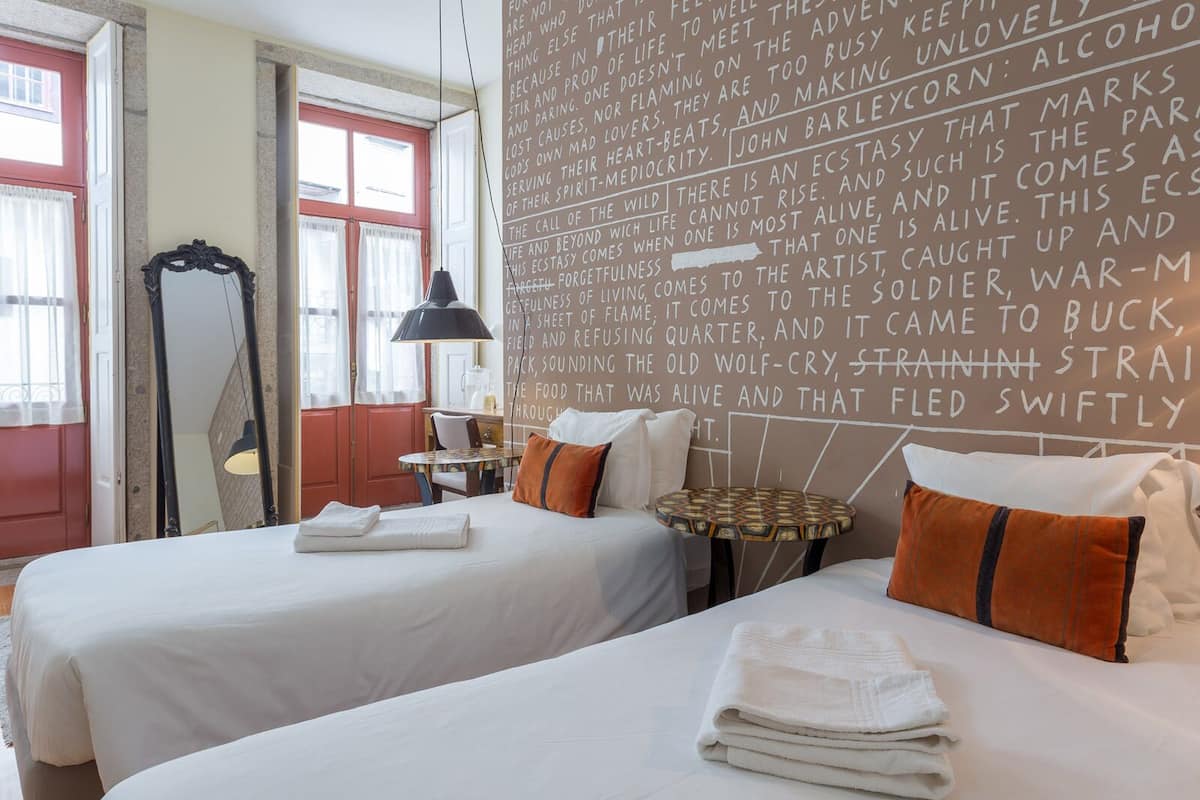 A hotel room with two beds, a mirror, a table, and a wall with text.