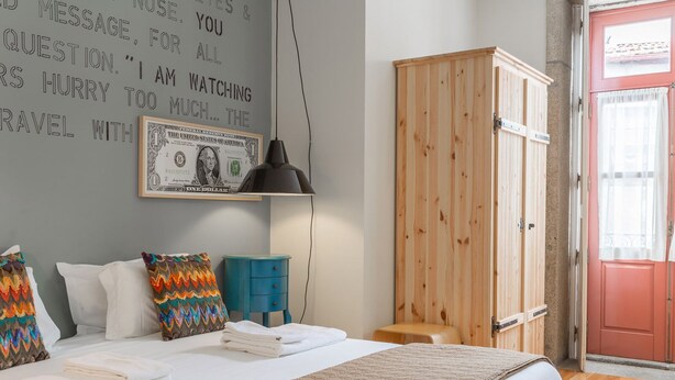 A bedroom with a bed, pillows, a blue side table, a wooden wardrobe, and a wall with a dollar bill artwork. - The Poets Inn (Porto)