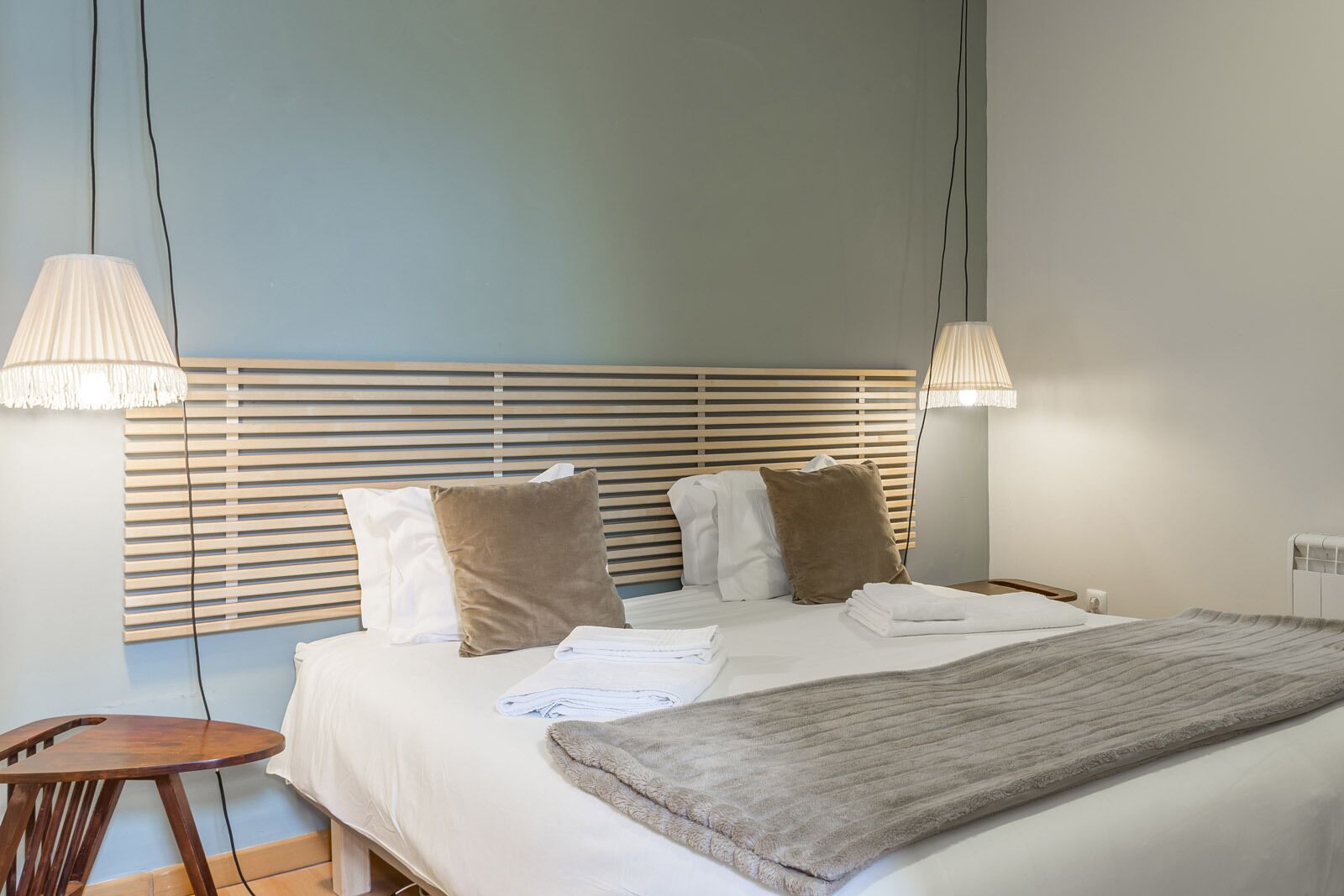 A neatly made bed with a headboard, two bedside lamps, and a bedside table with a lamp.
