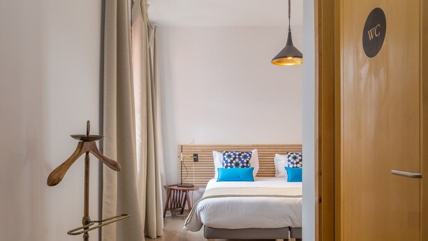 A hotel room with a bed, a bedside table, a lamp, and a door with a WC sign. - The Poets Inn (Porto)