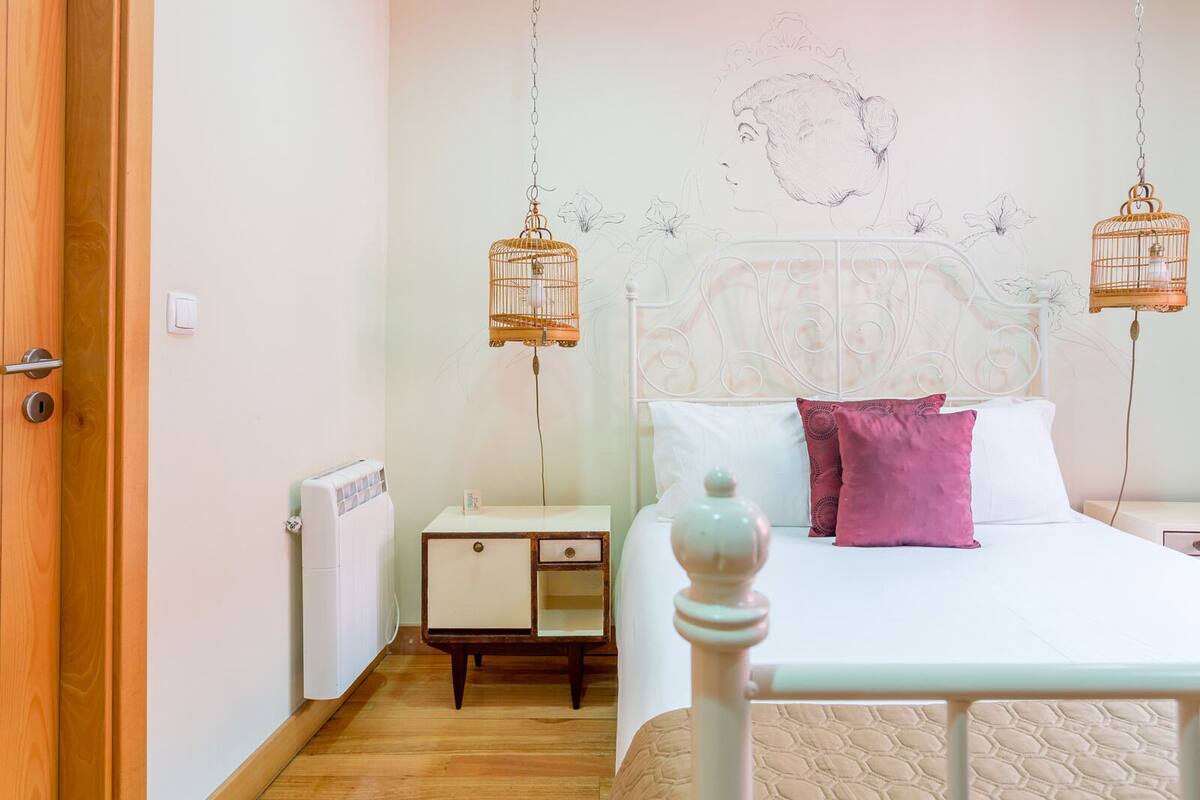 A bedroom with a bed, a nightstand, a dresser, and two wall-mounted birdcages.
