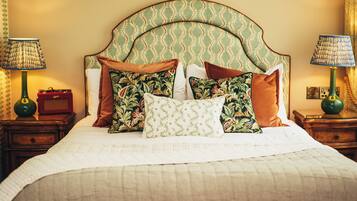 Una cama bien hecha con almohadones estampados y un cabecero verde. Hay dos mesitas de noche, una con lámparas y un pequeño reloj.