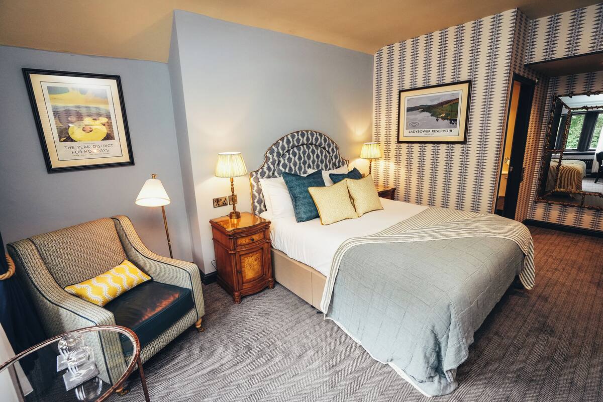 A hotel room with a bed, a chair, a nightstand, and a mirror.