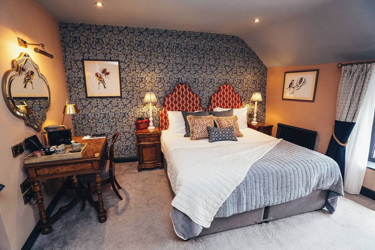 A bedroom with a large bed, a desk with a chair, a dresser, and a mirror.